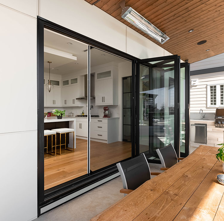 Indoor-outdoor kitchen featuring black-framed folding glass doors with retractable screens and wooden dining table