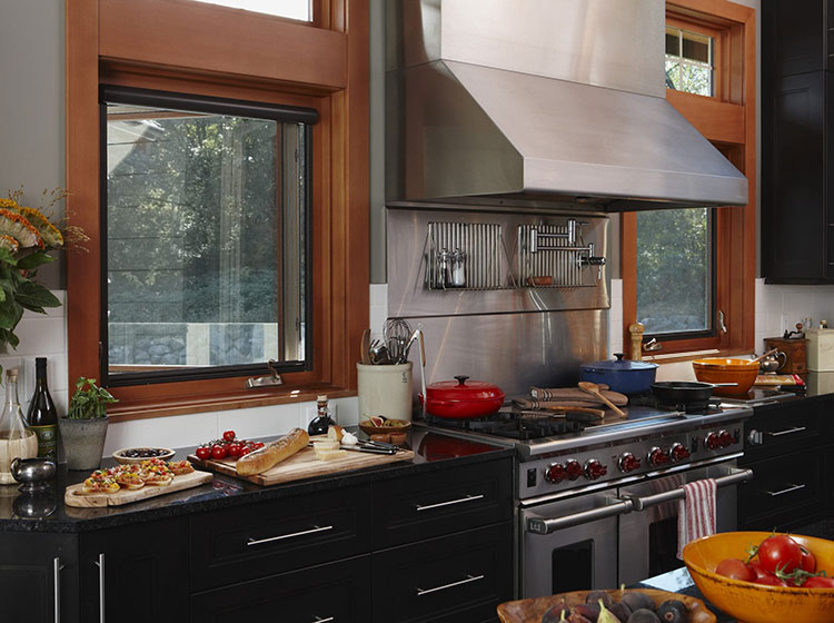 Modern kitchen with wood-framed casement windows, featuring black counters and stainless steel appliances